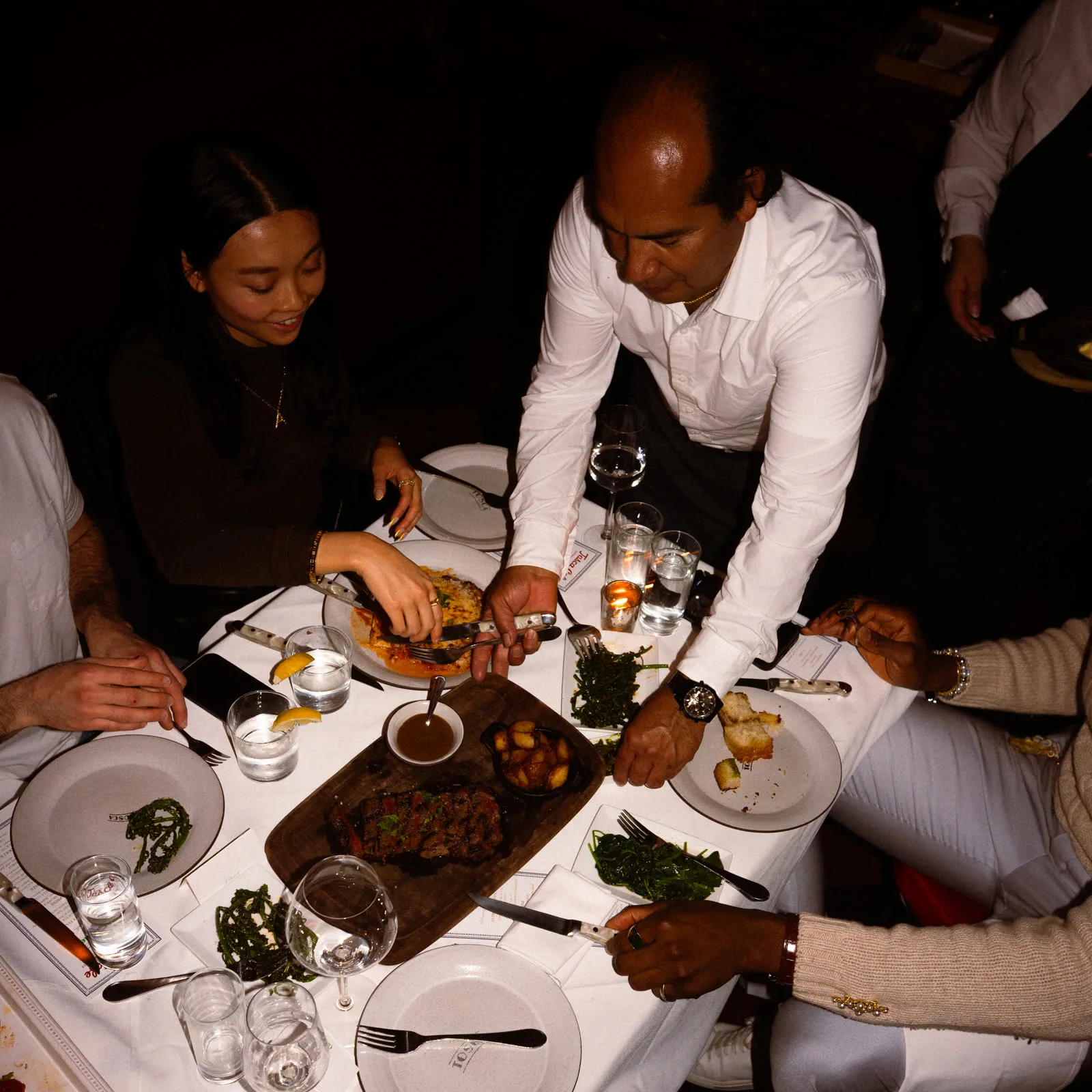 A server presenting a steak course tableside to guests at a Redamancy dinner.